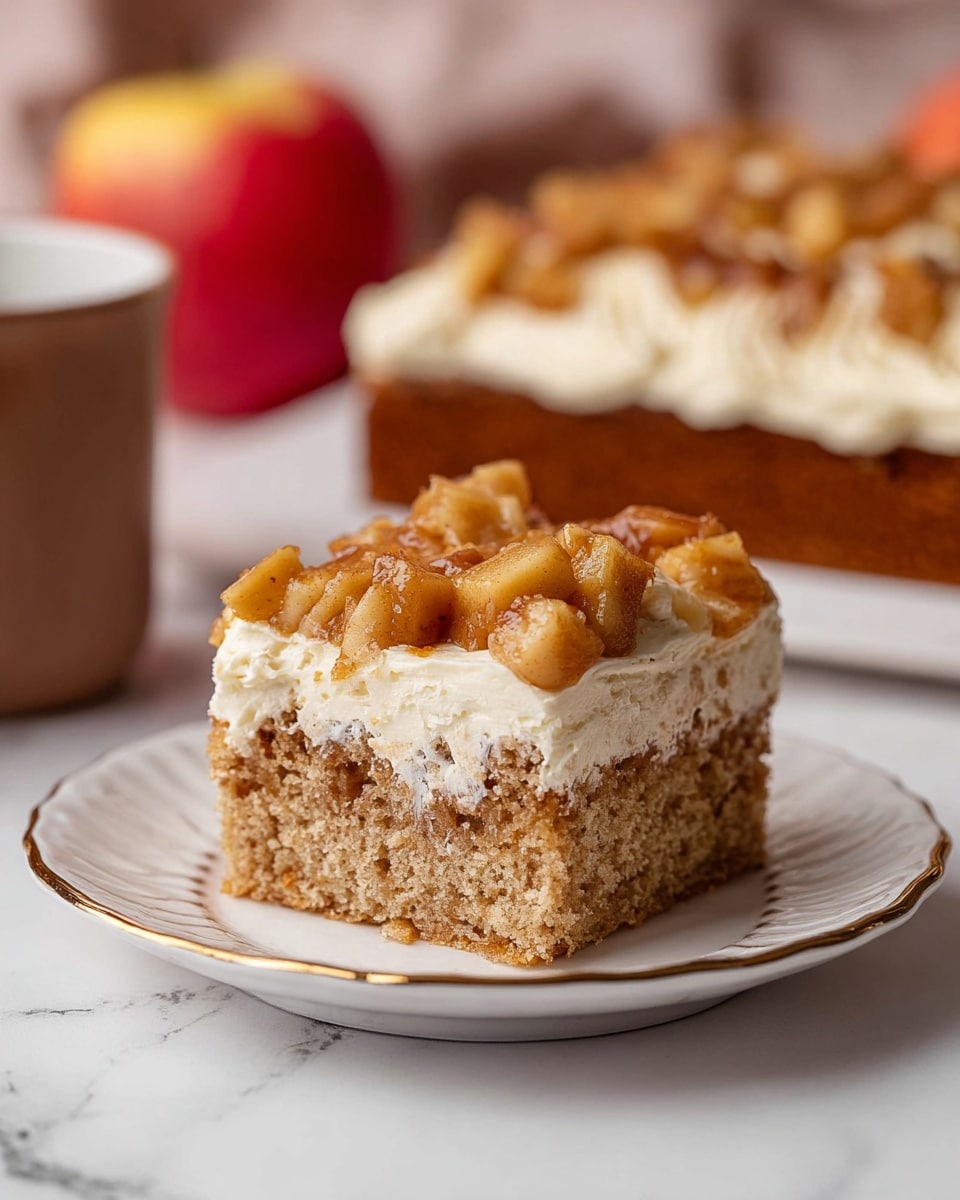 A square piece of cake is shown with three layers: the bottom layer is a light brown, soft, and slightly porous cake; the middle layer is a thick, creamy, off-white frosting; and the top layer has small chunks of cooked apples in a golden brown color, spread evenly. The cake piece sits on a white plate with a scalloped edge and a thin gold rim, all placed on a white marbled surface. In the blurred background, a matching cake with the same layers and a red apple are visible along with a brown mug. Photo taken with an iphone --ar 4:5 --v 7