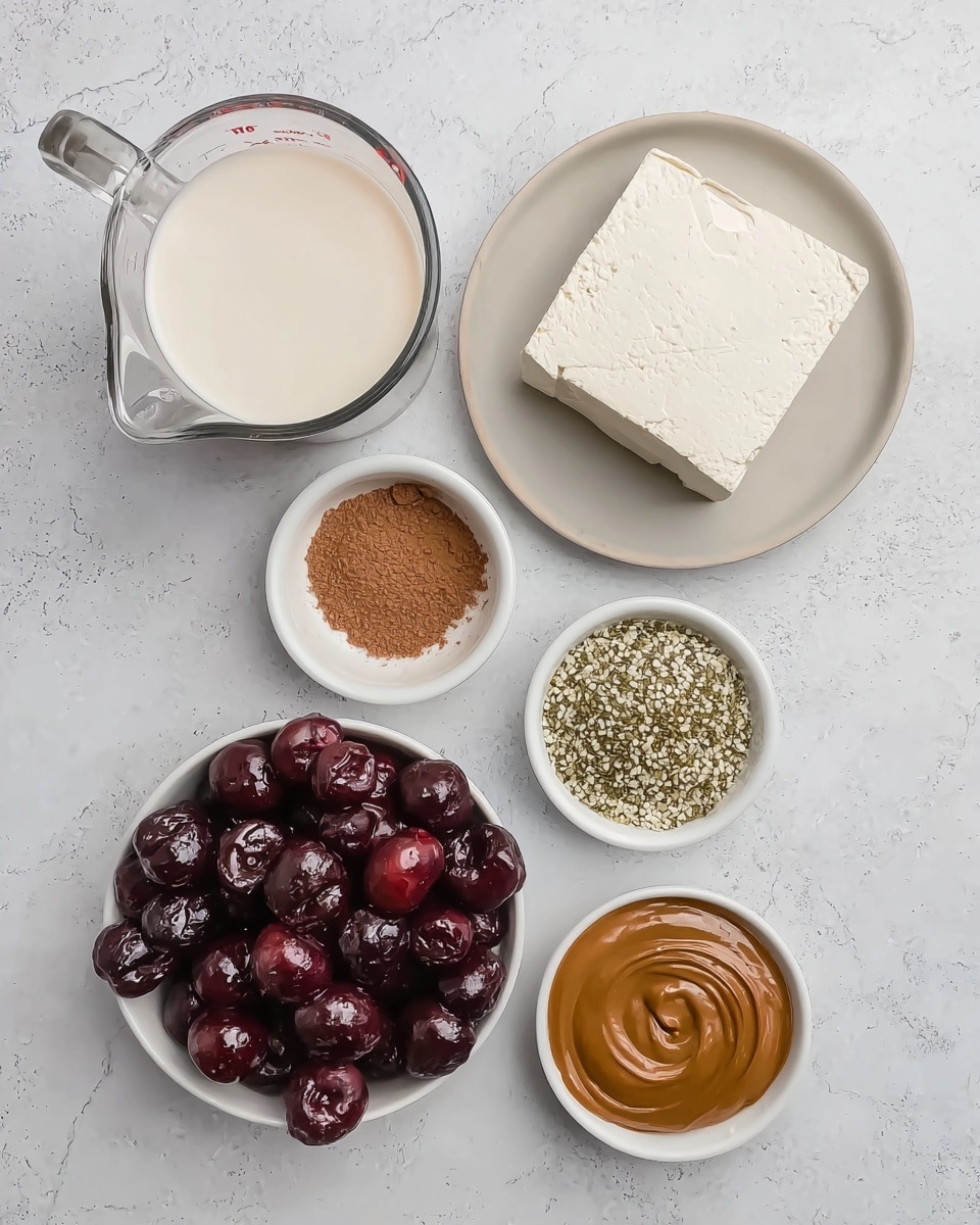 A clear glass measuring cup filled nearly to the top with white liquid is positioned on the left side over a white marbled surface. Next to it on the right, a white plate holds a block of plain white tofu. Below the tofu, three small white bowls are arranged in a vertical row: the top one holds light brown cocoa powder with a fine texture, the middle one contains light green and white hemp seeds, and the bottom bowl has smooth, shiny brown peanut butter with swirling patterns. At the bottom left, a white bowl is filled with dark red and purple frozen cherries, showing a mix of shiny and frosted surfaces. The photo taken with an iphone --ar 4:5 --v 7