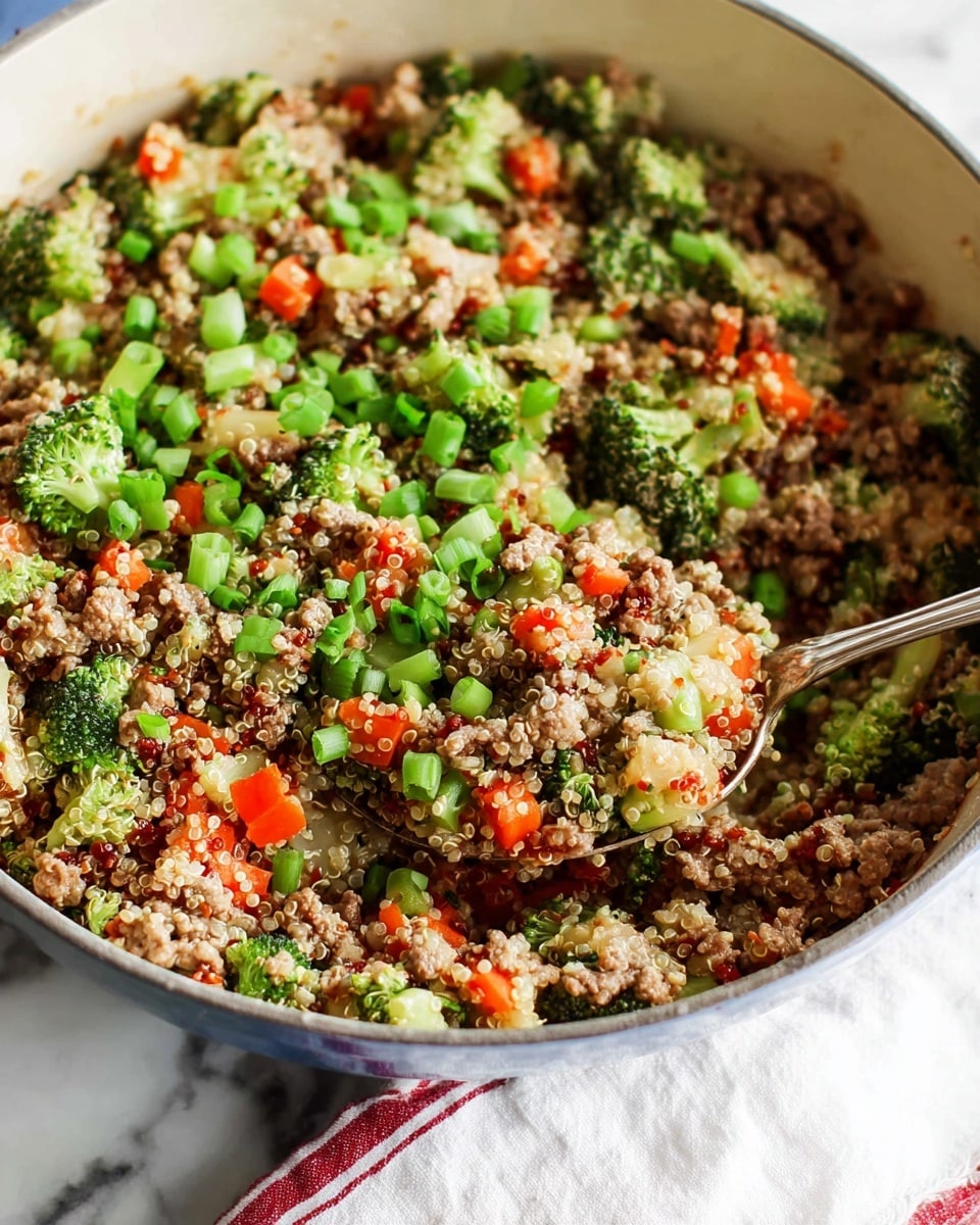 A close-up of a deep white pot filled with a mixed quinoa dish. The dish has three main layers: small green broccoli florets, light tan quinoa grains, and light brown ground meat mixed evenly throughout. There are also small diced orange carrots and chopped green onions sprinkled on top and mixed in. A silver spoon scoops up a portion from the pot showing the texture of the mixed ingredients. The background is a white marbled surface with subtle patterns visible, and a white cloth with faint red stripes lies under the pot's handle. Photo taken with an iphone --ar 4:5 --v 7