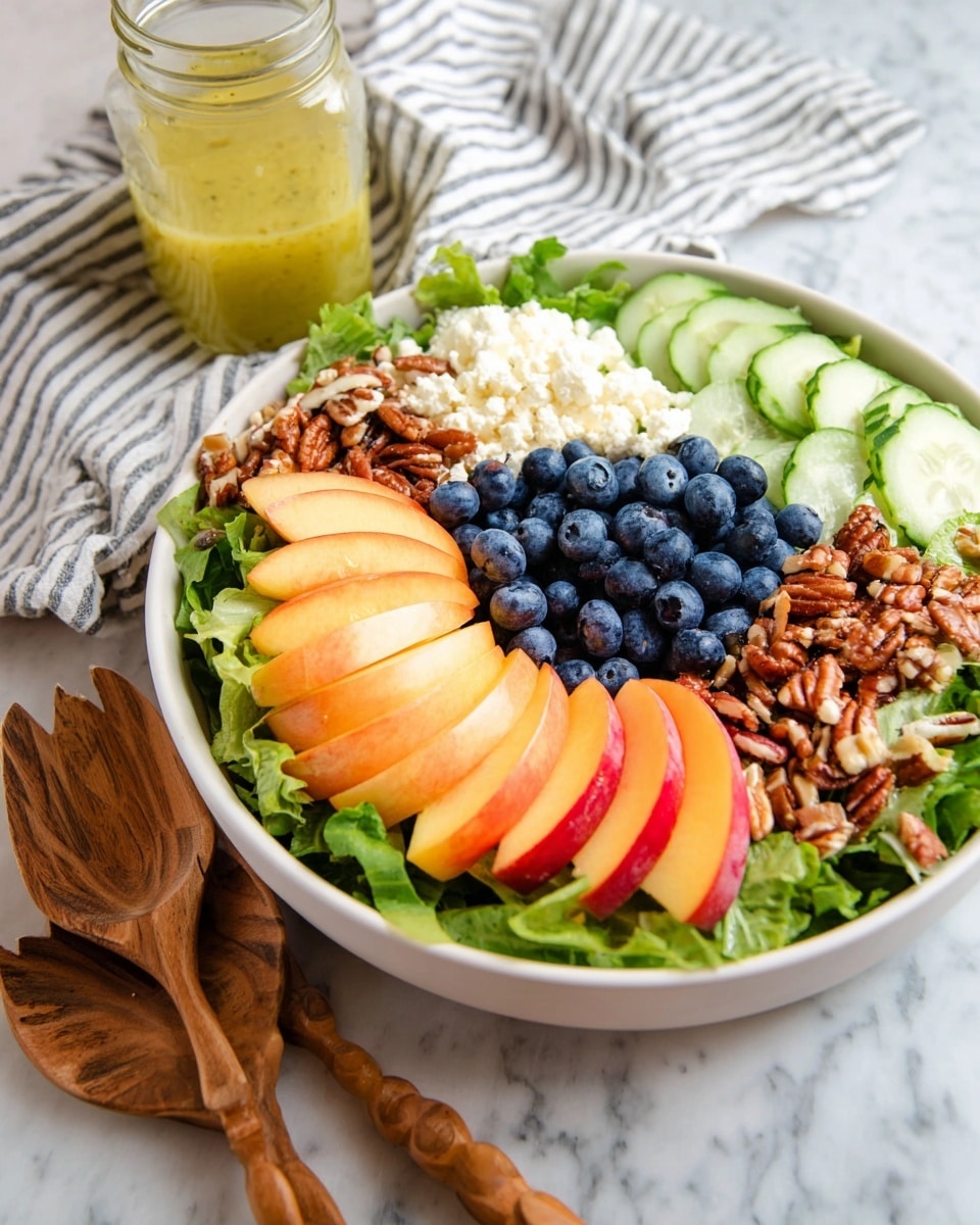 A white bowl filled with a fresh salad on a white marbled surface, layered with green leafy lettuce at the base. On top, there are thin slices of light pink and orange peach or nectarine arranged in a neat fan shape on one side. Next to the peaches, there is a pile of bright blue blueberries. Beside the blueberries, there is a cluster of chopped brown pecans. Next to the pecans, there is a pile of crumbly white cheese. Behind the cheese, there are sliced green cucumber rounds. In the background, a glass jar with yellow salad dressing and a striped cloth napkin can be seen. A carved wooden spoon and fork rest on the white marbled surface next to the bowl. Photo taken with an iphone --ar 4:5 --v 7