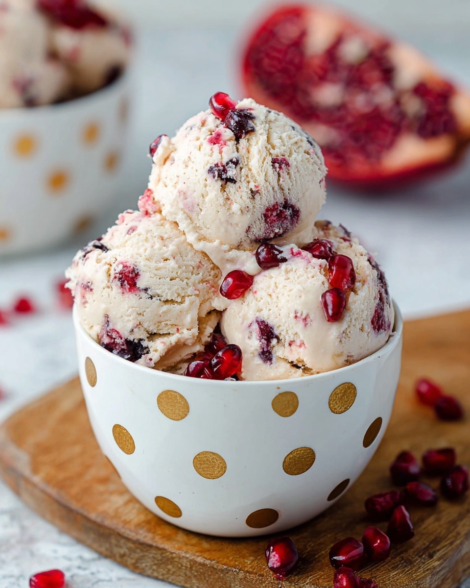 Three scoops of pale creamy ice cream with dark and bright red pomegranate seeds mixed inside each scoop sit in a white cup with gold polka dots. The ice cream texture is soft and slightly crumbly with juicy, shiny pomegranate seeds scattered on top and inside. The cup rests on a wooden board with some bright red seeds spilled around. In the blurry background, a half pomegranate with seeds and another white cup with gold polka dots filled with more scoops of the same ice cream are seen. The surface is a white marbled texture. photo taken with an iphone --ar 4:5 --v 7