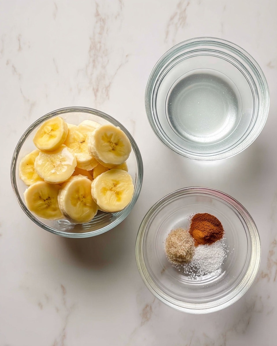 The image shows three clear glass bowls placed on a white marbled surface. The bowl on the left is filled with thick banana slices, light yellow with soft texture. The bowl on the top right contains clear water with smooth still surface. The bowl at the bottom right has small amounts of three dry powder spices: reddish-brown cinnamon, white granulated salt, and white pepper. All bowls are round and transparent, neatly arranged in a triangle shape. Photo taken with an iphone --ar 4:5 --v 7