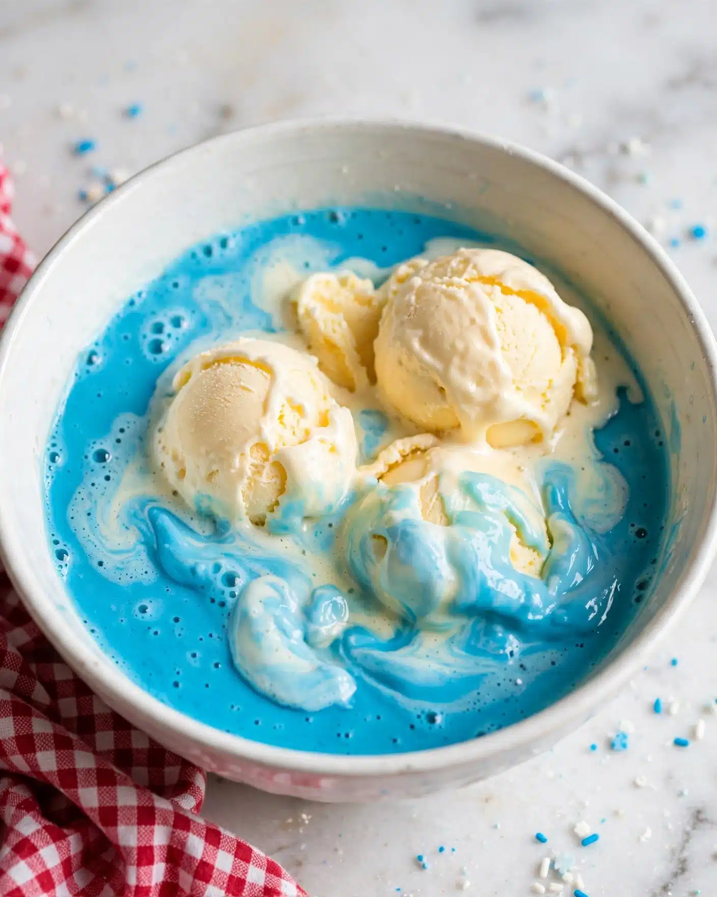 A white bowl filled with two distinct layers: the bottom layer is a bright turquoise blue, smooth and slightly thick, while the top layer shows several scoops of creamy pale yellow ice cream melting into the blue base, creating soft swirls and light blue patches. The bowl sits on a white marbled surface, and the creamy texture of the ice cream contrasts with the smooth, liquid consistency of the blue layer below. photo taken with an iphone --ar 4:5 --v 7