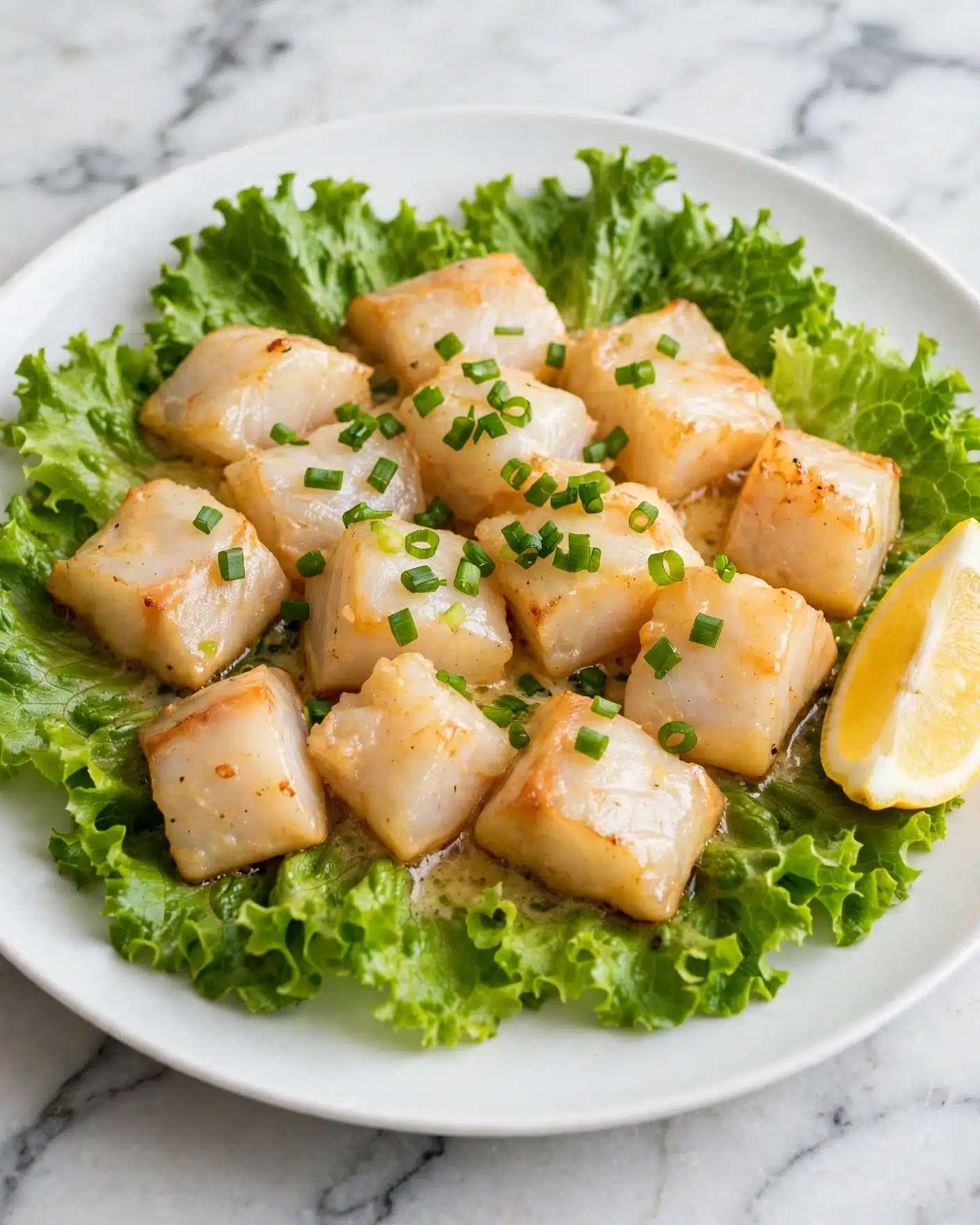 The dish is served on a white plate with a base layer of fresh green lettuce leaves arranged in a circular pattern. On top, there is a thick layer of white and red seafood pieces that look tender and slightly shiny. Small chopped green onions are scattered evenly over the seafood, adding a pop of green color. A wedge of bright yellow lemon sits on the edge of the plate, opposite the lettuce, adding a fresh accent. The white marbled surface beneath complements the colors of the dish. photo taken with an iphone --ar 4:5 --v 7