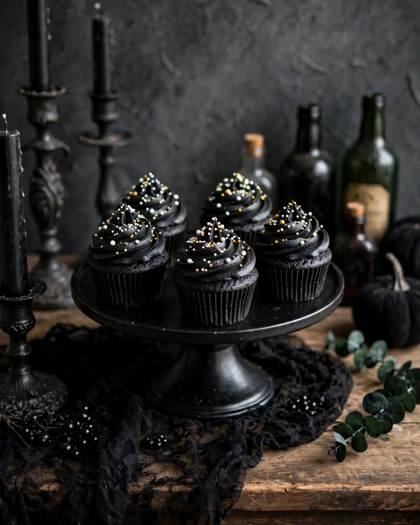 Black Velvet Cupcakes with Black Cocoa Buttercream Recipe 5 This image shows a group of black cupcakes arranged on a black cake stand and wooden surface, each cupcake has one layer of dark black cake and a thick swirl of black frosting on top. The frosting is decorated with small round white and gold sprinkles evenly spread over the swirled top. The background is a dark textured gray, with some black candle holders and vintage bottles adding a mysterious, moody feel. The overall look is rich, dark, and stylish. photo taken with an iphone --ar 4:5 --v 7