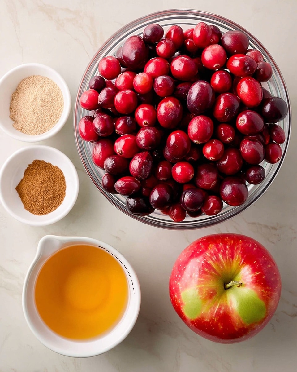 A clear glass bowl filled with bright red cranberries sits near the center on a white marbled surface, surrounded by three small white bowls holding spices—one with a light brown powder, another with a darker brown powder, and the third a ½ cup measure filled with a beige granulated ingredient. Below the cranberries is a fresh red apple with yellow-green tones near the stem, and next to it a white measuring cup with a golden liquid inside. The simple arrangement shows fresh and dry ingredients ready to be mixed. photo taken with an iphone --ar 4:5 --v 7